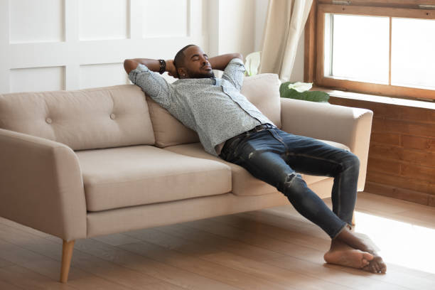 istock Happy millennial barefoot black guy daydreaming on sofa. 1177334829