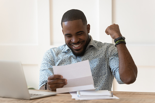 Happy euphoric young african american guy received paper report, university admission letter, celebrating important goal achievement, banking loan approval, full credit repayment, lottery win notice.