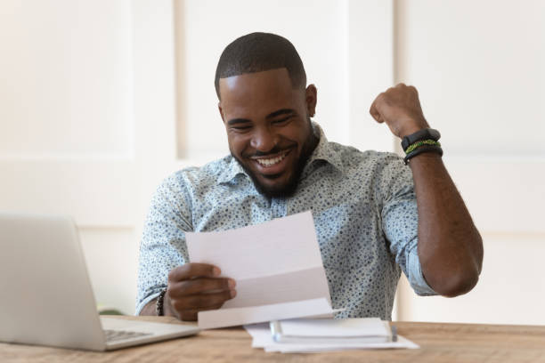 Happy african american guy received banking loan approval. Happy euphoric young african american guy received paper report, university admission letter, celebrating important goal achievement, banking loan approval, full credit repayment, lottery win notice. wages stock pictures, royalty-free photos & images