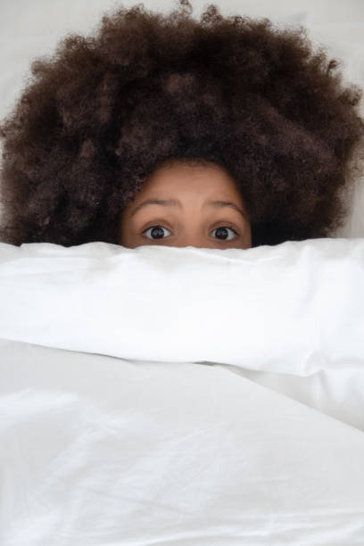 istock Top view close up scared black kid hiding under duvet. 1177334934