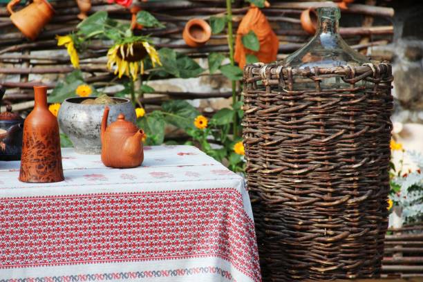 istock the table in the yard is covered with a white tablecloth with a red stripe, pottery and various jugs of clay, a large wicker basket on the background of a fence of branches 1177344222