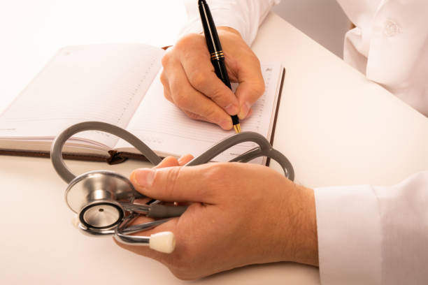 istock The doctor sits in an office at a white table, makes notes in a notebook, a stethoscope lies nearby, view from above. Close up 1177365468