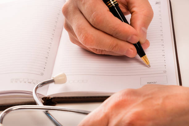 istock The doctor sits in an office at a white table, makes notes in a notebook, a stethoscope lies nearby, view from above. Close up 1177365610