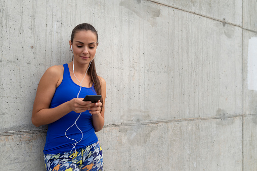 Portrait of Caucasian woman preparing music for running. She standing in front of wall.