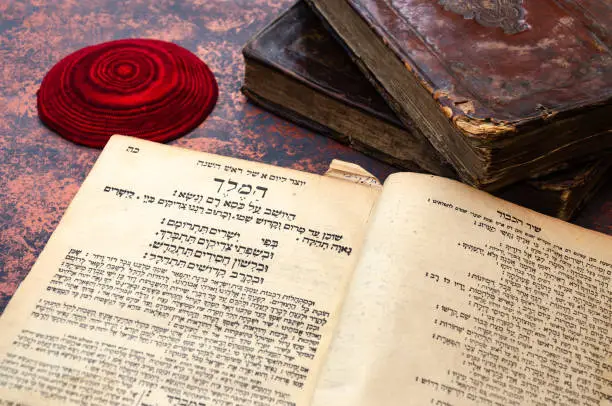 Jewish Bible. A stack of old leather-bound Jewish books with gold stamping and red knitted jewish bale. One book is open. Closeup of Hebrew text. Selective focus