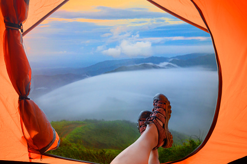 view from the tent of Legs of traveller laying relax in the morning, looking at flowing of mist in the mountain