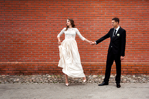 Newlyweds embracing next to red brick wall. Young wedding couple.