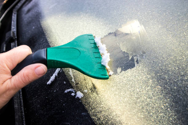 z bliska widok osoby ręcznie skrobanie lodu z przedniej szyby samochodu z skrobakem we wczesnych godzinach porannych jesienią w europie północnej. - frozen windshield cold car zdjęcia i obrazy z banku zdjęć