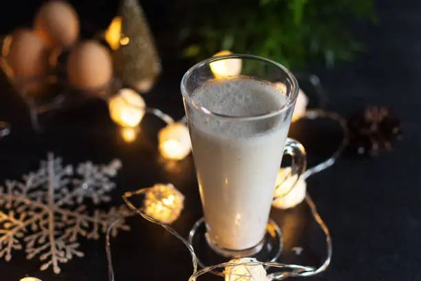 Fresh eggnog with cinnamon and nutmeg for christmas holiday with christmas decorations on dark background, low key.