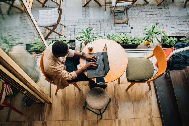 Young African man sitting in coffee shop and using laptop