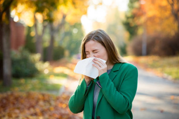 Sick young woman with cold and flu Sick young woman with cold and flu standing outdoors, sneezing, wiping nose with handkerchief, coughing. Autumn street background sinusitis photos stock pictures, royalty-free photos & images
