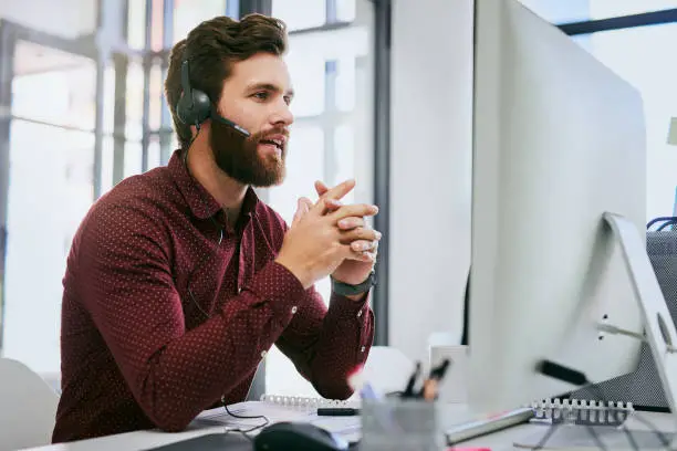 Cropped shot of a handsome young businessman sitting alone and wearing a headset while using a computer in the office