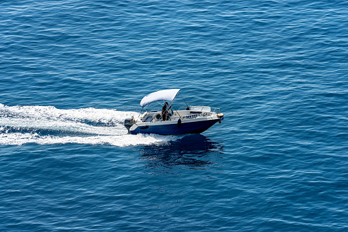 Vernazza, Liguria, Italy - July 22th, 2019: a small blue motor boat with one person on board runs fast in the blue Mediterranean sea with white wake, photographed from above. Cinque Terre, Liguria, Italia, south Europe