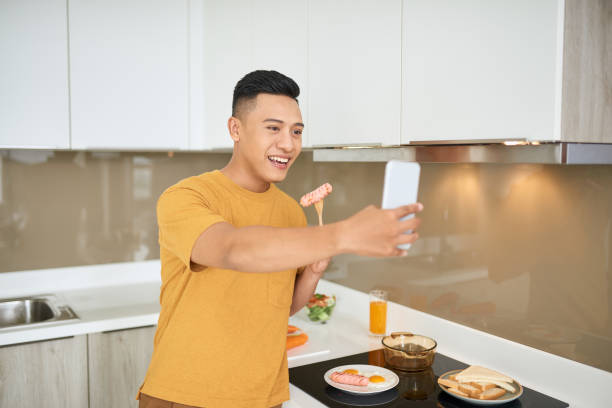 istock Handsome young man having breakfast while sitting at the kitchen, holding mobile phone 1177388804