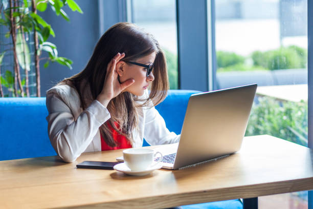 what? portrait of attentive beautiful stylish brunette young woman in glasses sitting, looking at her laptop screen on video call and try to hear or listen. - silence finger on lips businesswoman one person imagens e fotografias de stock