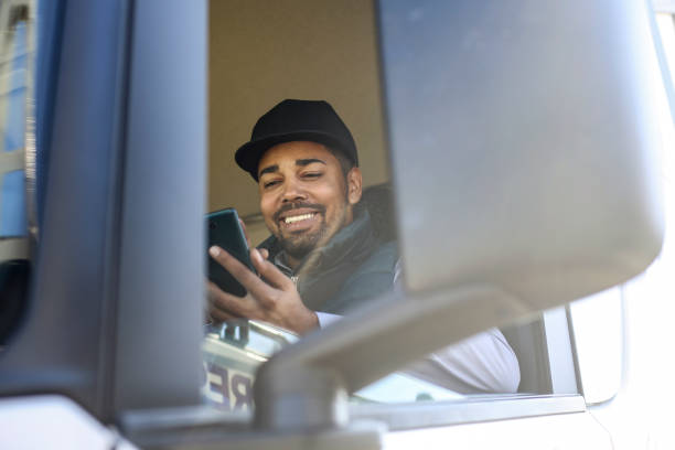Truck driver using a mobile app Truck driver using a phone. About 35 years old, African male. trucking photos stock pictures, royalty-free photos & images