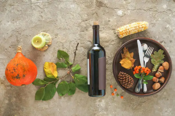 Thanksgiving greeting card. Pumpkin, a bottle of wine and a serving of plates on a concrete gray background. Flat lay, top view