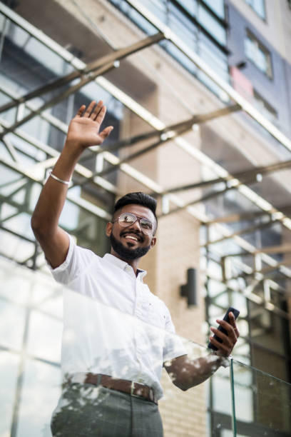 istock Indian businessman in eye glasses looking on copy space while standing against glass skyscraper waving hello to someone. 1177400201