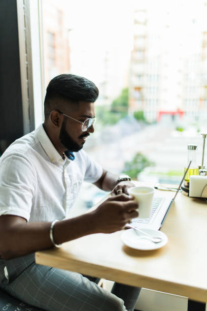 istock Indian man using laptop computer while drinking a cup hot milk tea, outdoor cafe. 1177400582