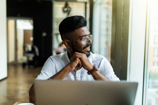 Young Asian Indian businessman using a notebook computer or laptop during office break at cafe, relaxing with a cup of coffee.