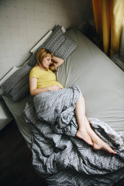 집에서 노란색 티셔츠에 임신 한 소녀 금발. 기적을 기다리고 있습니다. 임신. 사랑과 희망. 가벼운 방입니다. 침실의 침대에 누워 있습니다. 회색 침구 - human pregnancy miracle bed love 뉴스 사진 이미지