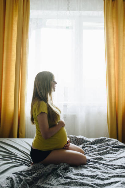 집에서 노란색 티셔츠에 임신 한 소녀 금발. 기적을 기다리고 있습니다. 임신. 사랑 희망. 회색 침구. 침실에 침대에 누워 - human pregnancy miracle bed love 뉴스 사진 이미지