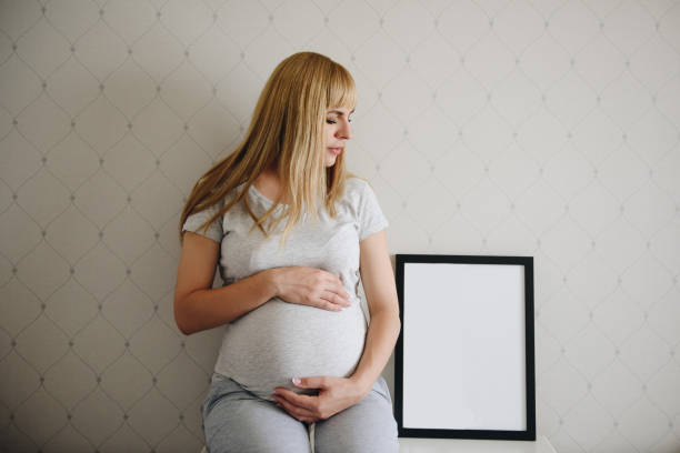 自宅で灰色のパジャマで妊娠中の女の子のブロンド。奇跡を待ってる妊娠。愛と希望明るい部屋。テキストの枠 - human pregnancy miracle bed love ストックフォトと画像