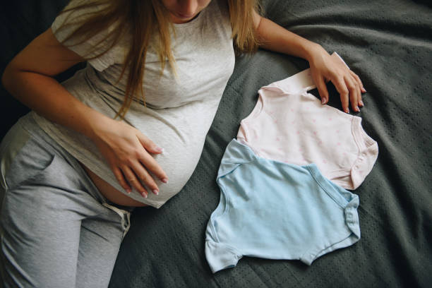 임신 한 소녀 금발의 회색 잠옷 에 집에서 기적을 기다리고 있습니다. 임신. 사랑과 희망. 가벼운 방입니다. 텍스트의 프레임입니다. 회색 침구. 신생아를위한 옷. 소년 또는 소녀 - human pregnancy miracle bed love 뉴스 사진 이미지