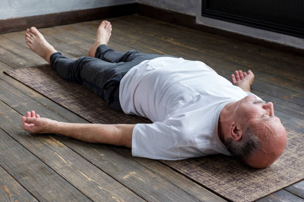 homem latino-americano maduro no pose do cadáver da ioga no assoalho de madeira. - reclining buddha - fotografias e filmes do acervo