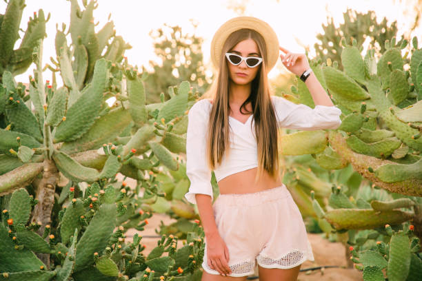 istock Young girl in hat and sunglasses posing against cactuses 1177409358