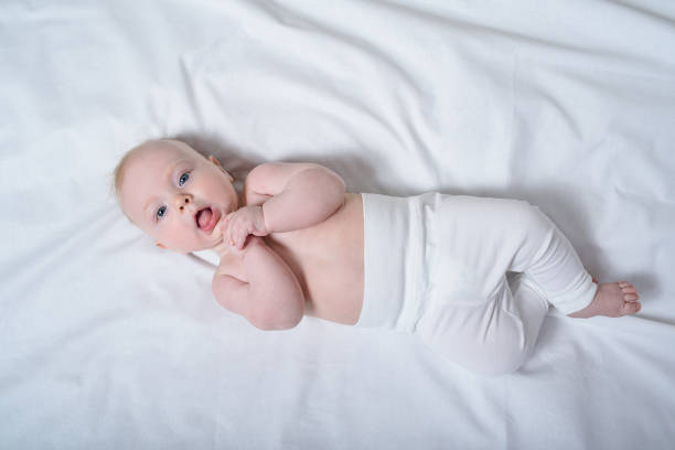 istock Cute blond baby with a naked torso lying on white sheets. Top view 1177410763