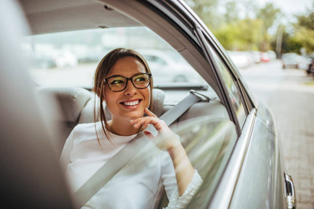 ritratto di una giovane donna felice sul sedile posteriore dell'auto che guarda fuori dal finestrino. - taxi travel business women foto e immagini stock