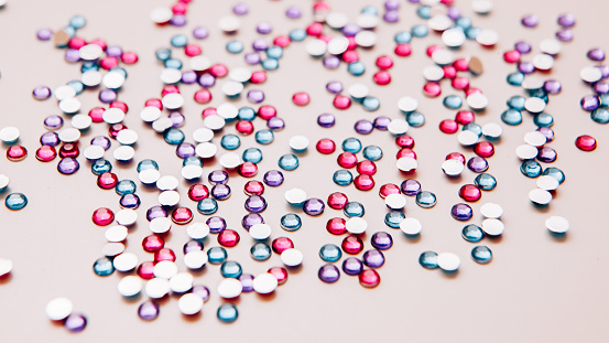 Fashion craft. DIY clothing decoration. Multicolor rhinestones scattered on pink toned background.