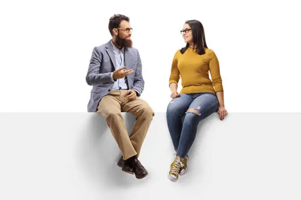 Full length shot of a bearded man talking to a young female seated on a banner isolated on white background