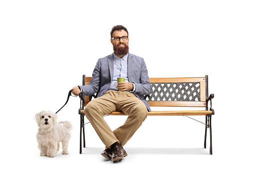 Bearded man sitting on a bench with a cup of take away coffee and a dog on a leash isolated on white background