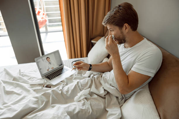 Man making a video call to his doctor Sick young male blowing his nose talking to a doctor blowing nose photos stock pictures, royalty-free photos & images