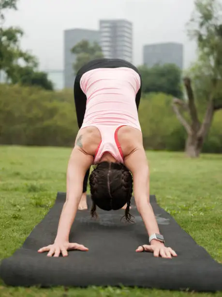 Photo of Young latin woman doing downward-facing dog yoga position outdoors