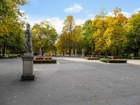 Square and alley with sculptures among yellow trees in the Saxon Garden in Warsaw, Poland. Beautiful autumn landscape of a city public park on October sunny day, background with copy space