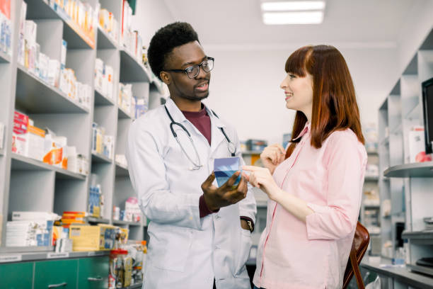 istock Handsome African male pharmacist talking with a beautiful female client in modern light pharmacy. 1177434458