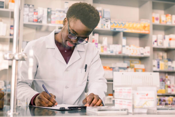 Portrait of a happy African American pharmacist writing prescription at workplace in modern pharmacy Portrait of a happy African American pharmacist writing prescription at workplace in modern pharmacy. pharmacy tech stock pictures, royalty-free photos & images