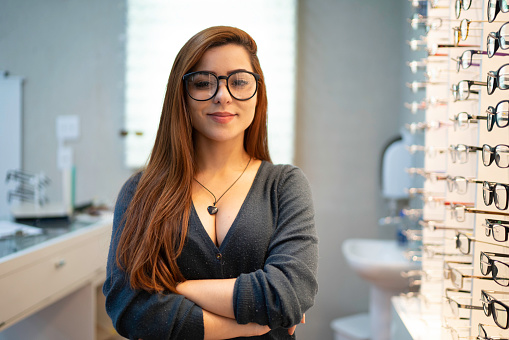 Portrait of young optometrist or customer with arms crossed in an optical store