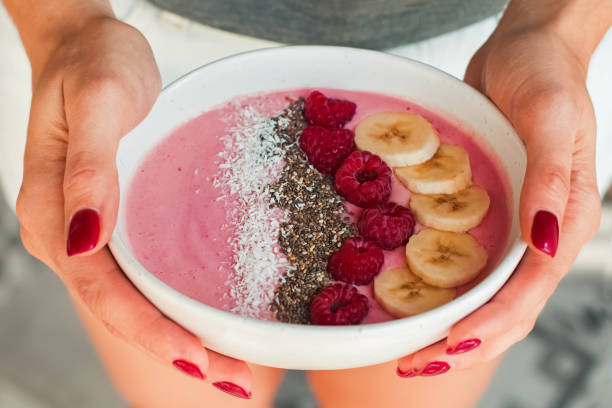 istock Woman's hands holding smoothie bowl with raspberries and bananas close-up. 1177448754