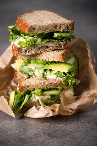 Healthy sandwich with green ingredients, avocado, cucumber and fresh salad, wrapped in brown paper. Gourmet conception. stock photo