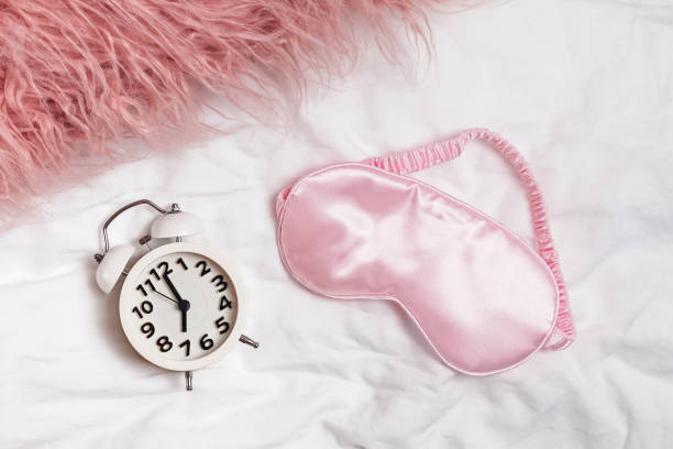 istock Alarm clock and pink slipping mask on the bed, 1177451221