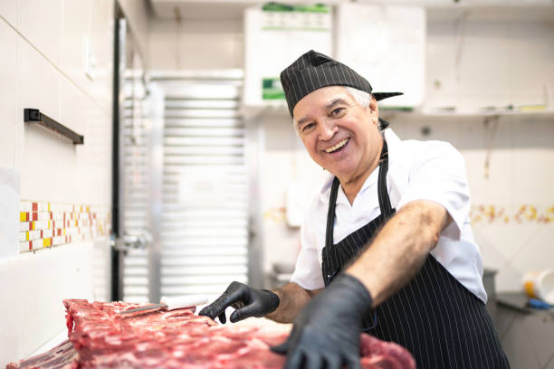 porträt eines metzgers, der in der metzgerei ein stück rotes fleisch schneidet - butcher meat butchers shop steak stock-fotos und bilder