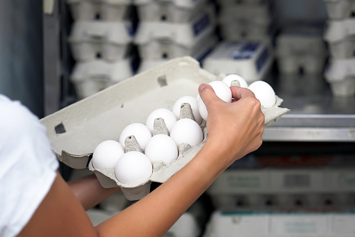 Hands woman with packages of white eggs in the store or supermarket. Woman buys eggs. Buying eggs at the grocery store