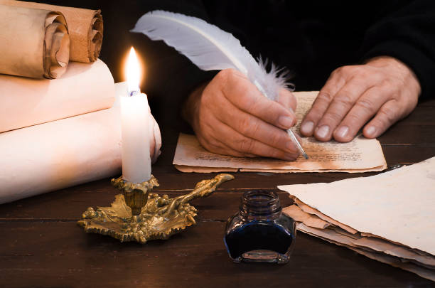 uma vela iluminada contra o fundo de rolos borrados, mão do escritor, livros e pena do pássaro - scribe - fotografias e filmes do acervo