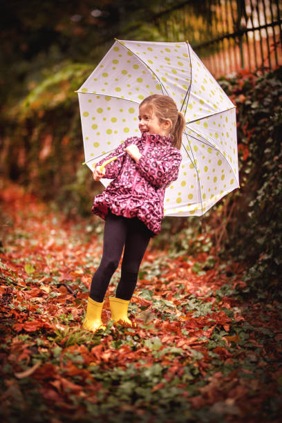 istock Happy child girl with an umbrella and rubber boots 1177458389