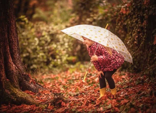 istock Happy child girl with an umbrella and rubber boots 1177458395