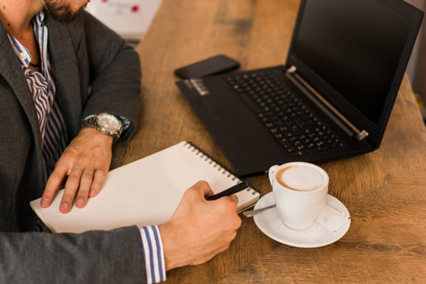 istock Young businessman is writing in his notebook while he is taking a coffee in a pub. Close up 1177459836
